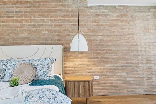 bedroom featuring brick wall and wood finished floors