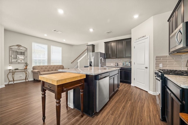 kitchen featuring sink, appliances with stainless steel finishes, a kitchen island with sink, light stone countertops, and dark hardwood / wood-style flooring