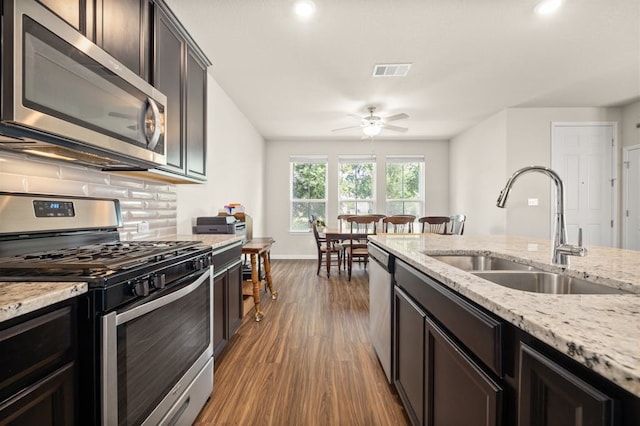 kitchen with sink, appliances with stainless steel finishes, dark hardwood / wood-style flooring, light stone countertops, and backsplash