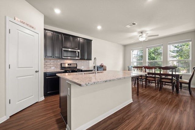 kitchen with dark hardwood / wood-style floors, sink, a kitchen island with sink, light stone counters, and stainless steel appliances