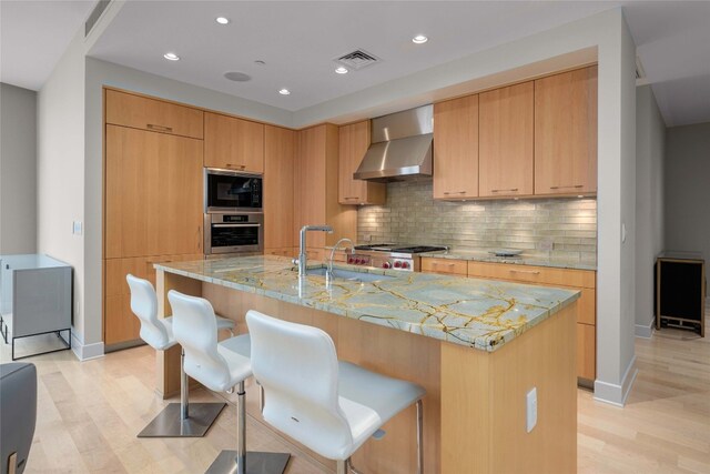 kitchen with a center island with sink, light hardwood / wood-style floors, wall chimney exhaust hood, and stainless steel oven