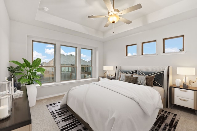 bedroom featuring ceiling fan, a tray ceiling, and light carpet