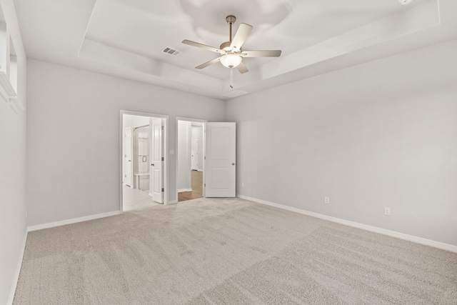 unfurnished bedroom with light carpet, ceiling fan, and a tray ceiling