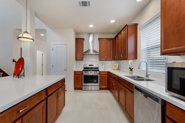 kitchen featuring wall chimney range hood, sink, appliances with stainless steel finishes, decorative backsplash, and decorative light fixtures