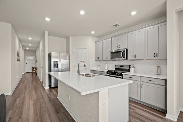 kitchen featuring appliances with stainless steel finishes, hardwood / wood-style flooring, tasteful backsplash, and an island with sink