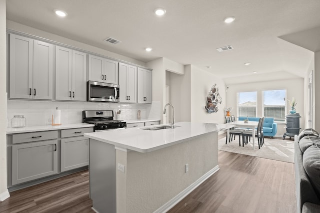 kitchen featuring sink, dark wood-type flooring, appliances with stainless steel finishes, backsplash, and a kitchen island with sink