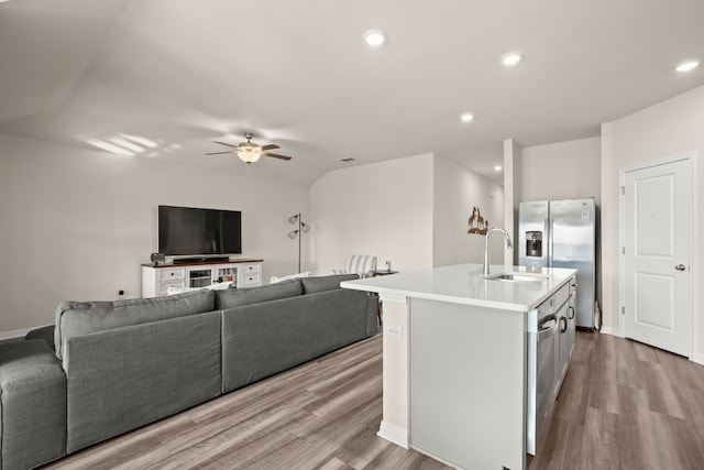 kitchen with ceiling fan, sink, vaulted ceiling, light hardwood / wood-style floors, and a kitchen island with sink