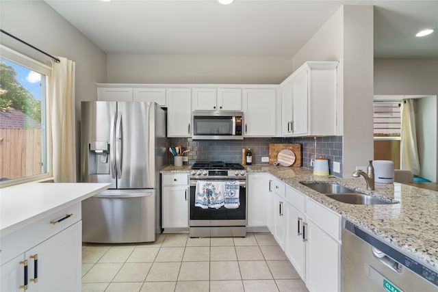 kitchen with appliances with stainless steel finishes, backsplash, light stone countertops, light tile patterned flooring, and white cabinetry