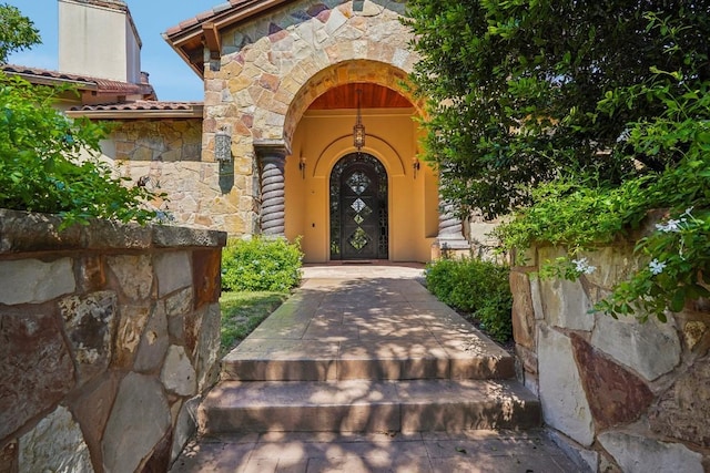 view of exterior entry with a tiled roof and stone siding