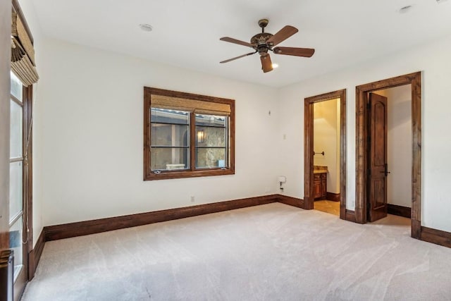 unfurnished bedroom featuring baseboards, ensuite bath, light carpet, and a ceiling fan