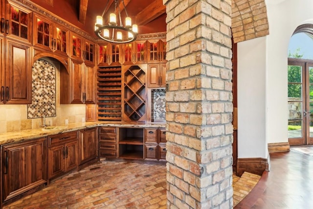 wine room featuring brick floor, baseboards, a sink, beamed ceiling, and a notable chandelier