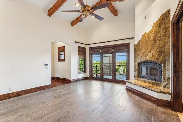 unfurnished living room featuring dark wood finished floors, baseboards, high vaulted ceiling, arched walkways, and beamed ceiling