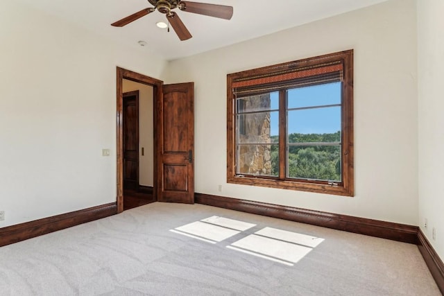 carpeted spare room featuring baseboards and ceiling fan