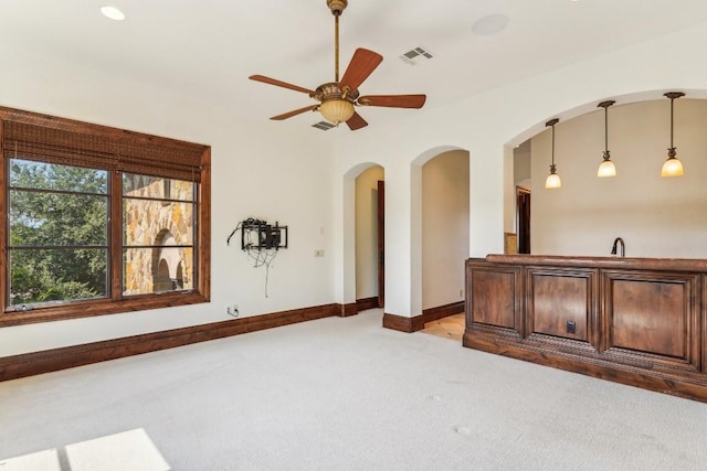 spare room featuring baseboards, visible vents, arched walkways, light colored carpet, and ceiling fan