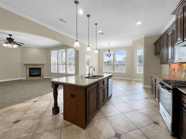 kitchen with sink, a kitchen island with sink, stainless steel appliances, light stone counters, and decorative light fixtures