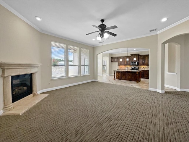 unfurnished living room with sink, ornamental molding, ceiling fan, a premium fireplace, and light carpet