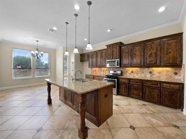 kitchen with sink, light stone counters, hanging light fixtures, stainless steel appliances, and a kitchen island with sink