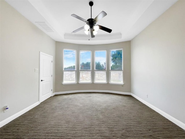 spare room featuring a raised ceiling, dark colored carpet, and ceiling fan