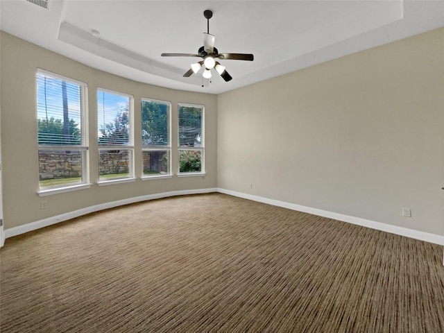 spare room with a tray ceiling, ceiling fan, and dark colored carpet