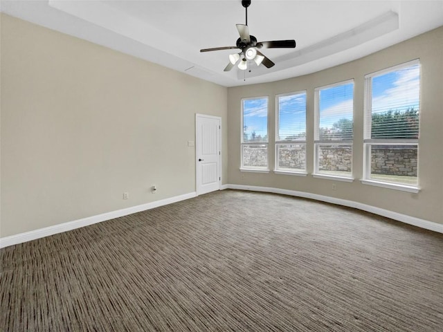 carpeted spare room with ceiling fan, a raised ceiling, and a healthy amount of sunlight