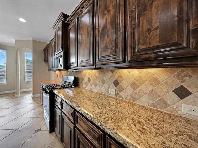 kitchen with light tile patterned floors, dark brown cabinets, stainless steel appliances, light stone counters, and decorative backsplash