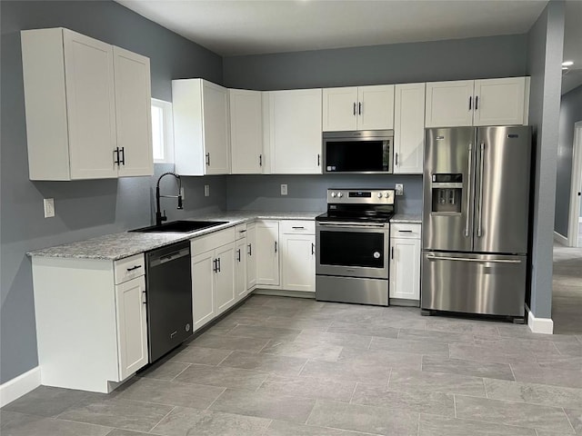 kitchen featuring a sink, baseboards, white cabinets, appliances with stainless steel finishes, and light stone countertops