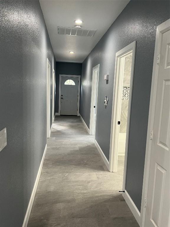 hallway featuring light wood-style floors, baseboards, visible vents, and a textured wall