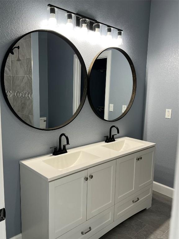 bathroom featuring a textured wall, a sink, baseboards, and double vanity