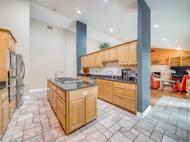 kitchen featuring stainless steel appliances, light brown cabinets, tasteful backsplash, dark stone counters, and a center island with sink