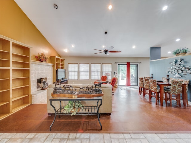 living room with a wealth of natural light, ceiling fan, built in shelves, and a stone fireplace