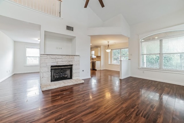 unfurnished living room featuring a stone fireplace, high vaulted ceiling, dark hardwood / wood-style floors, and ceiling fan