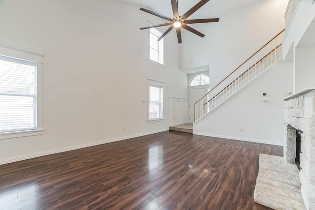 unfurnished living room featuring ceiling fan, a fireplace, dark hardwood / wood-style flooring, and a towering ceiling