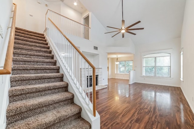 stairway with hardwood / wood-style flooring, a stone fireplace, high vaulted ceiling, and ceiling fan