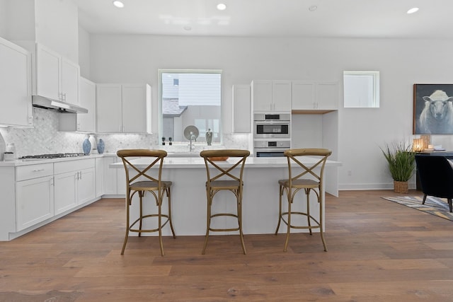 kitchen with a breakfast bar area, white cabinets, a center island, hardwood / wood-style floors, and appliances with stainless steel finishes