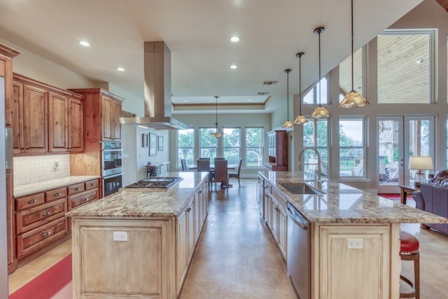 kitchen featuring tasteful backsplash, wall chimney range hood, light stone counters, a large island with sink, and sink