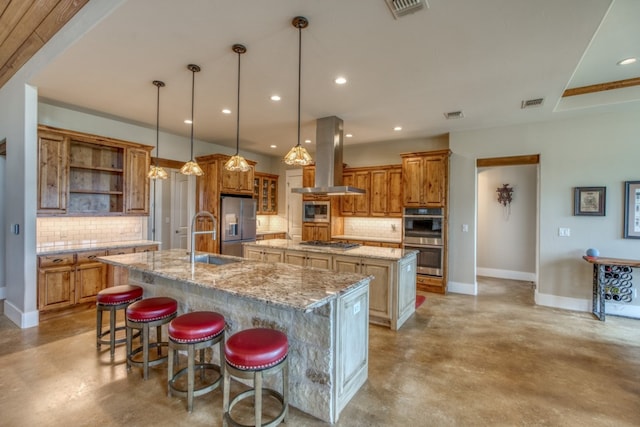 kitchen with appliances with stainless steel finishes, island range hood, sink, decorative backsplash, and a large island with sink