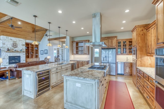 kitchen with wine cooler, ceiling fan, island exhaust hood, a stone fireplace, and a spacious island