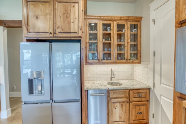 kitchen featuring backsplash, fridge, light stone counters, and sink