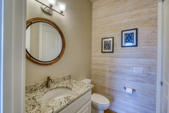 bathroom featuring vanity, wood walls, and toilet