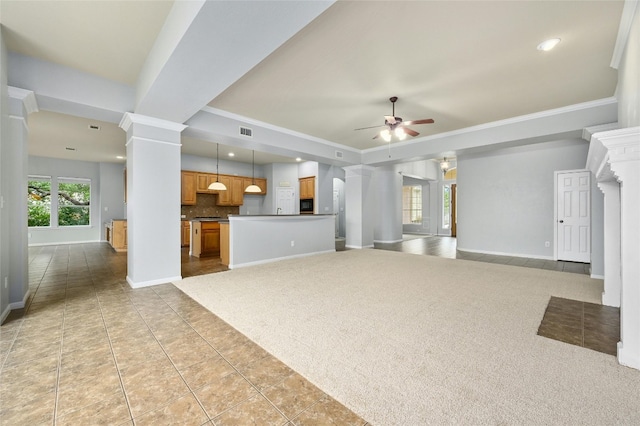 unfurnished living room with a tray ceiling, decorative columns, crown molding, light tile patterned flooring, and ceiling fan