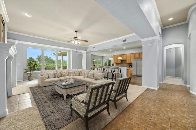 tiled living room with decorative columns, ceiling fan, and crown molding