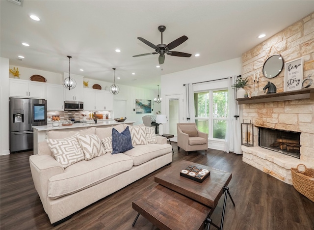 living room featuring a stone fireplace, dark wood-type flooring, and ceiling fan with notable chandelier