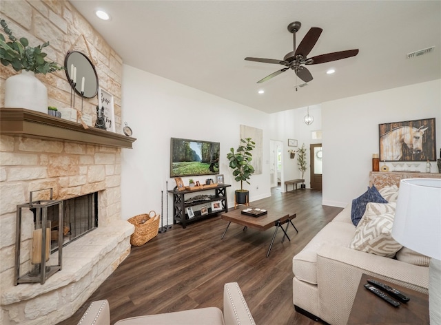 living room featuring dark wood-type flooring, ceiling fan, and a stone fireplace