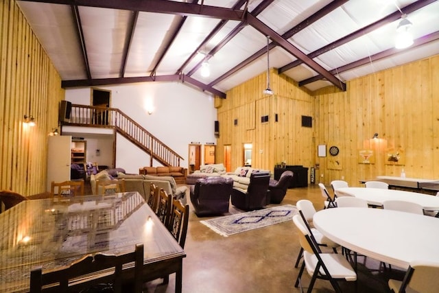 dining room featuring wooden walls, high vaulted ceiling, and concrete floors