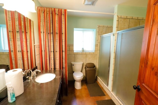 bathroom with a shower with door, vanity, tile walls, and toilet