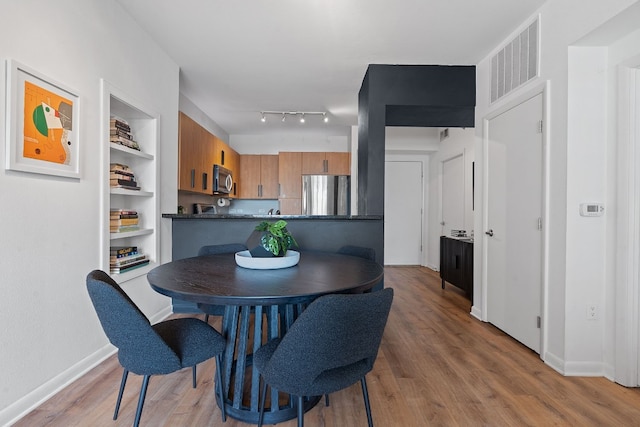 dining room with light wood-style flooring, built in shelves, visible vents, and baseboards