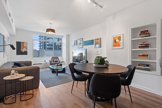 dining space with built in shelves, track lighting, baseboards, and wood finished floors