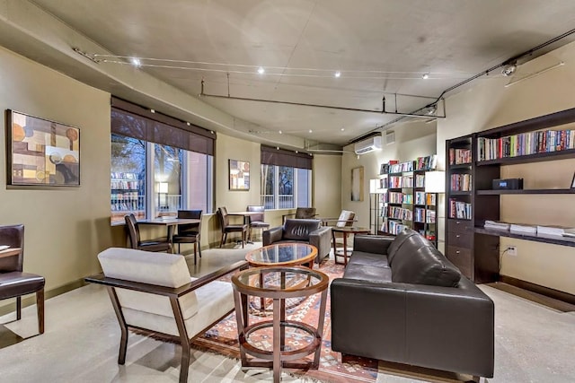 living area featuring concrete flooring, a wall mounted air conditioner, and baseboards