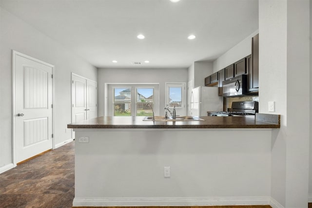 kitchen with recessed lighting, freestanding refrigerator, a sink, stove, and dark countertops