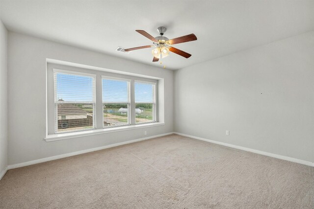 carpeted spare room with visible vents, baseboards, and ceiling fan